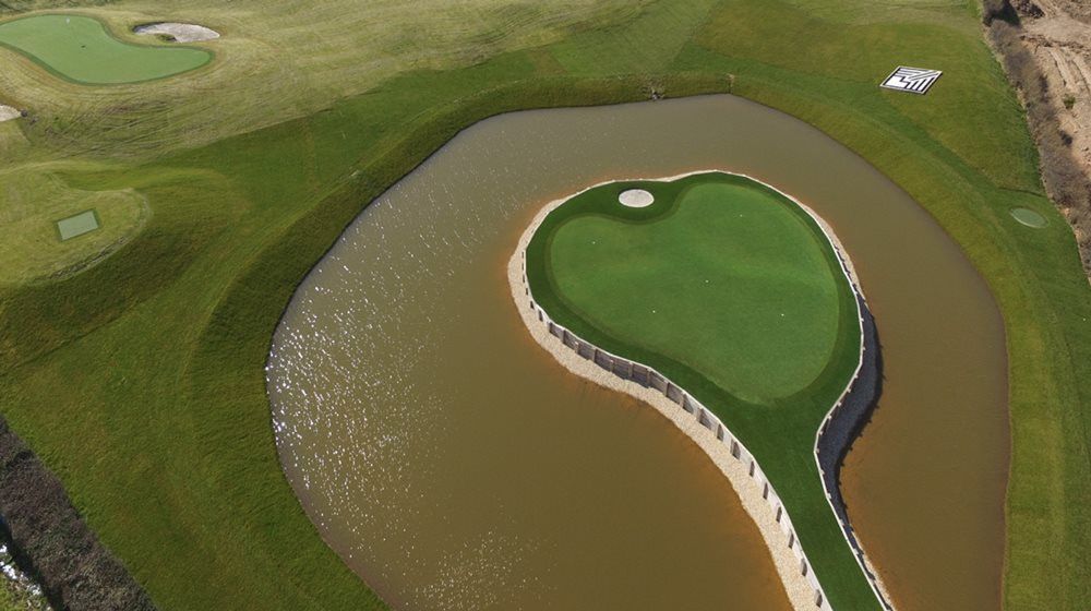 Phoenix Aerial view of a vibrant green synthetic grass island in a natural pond on a golf course